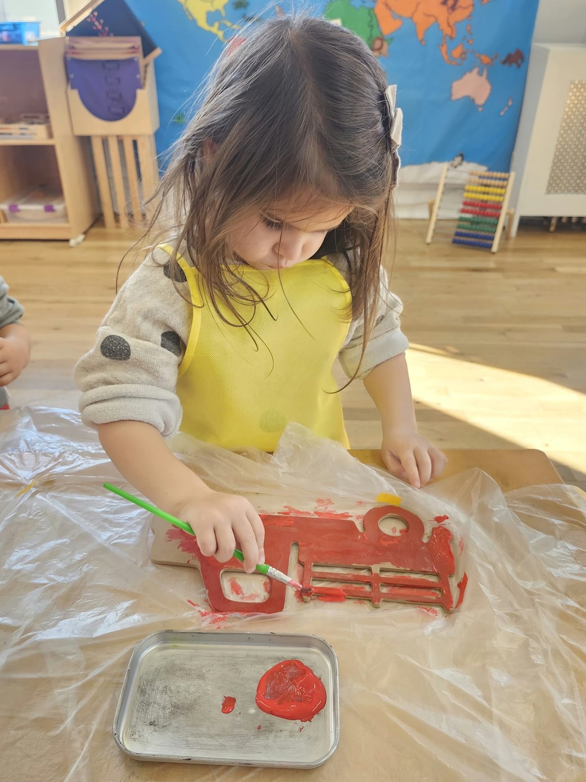 A child painting a wooden fire truck at the art table